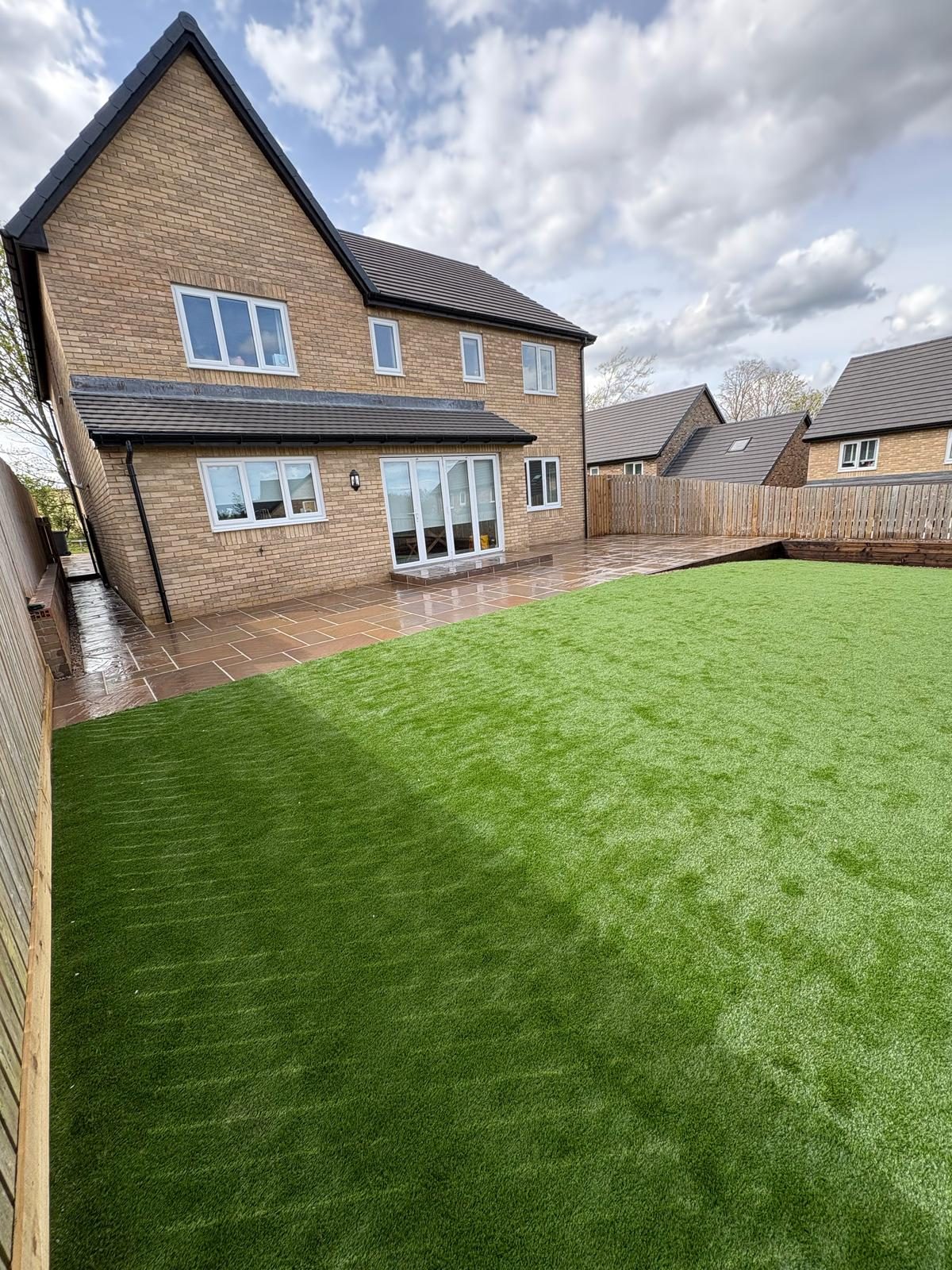 A new artificial lawn and sandstone terrace behind a new build house