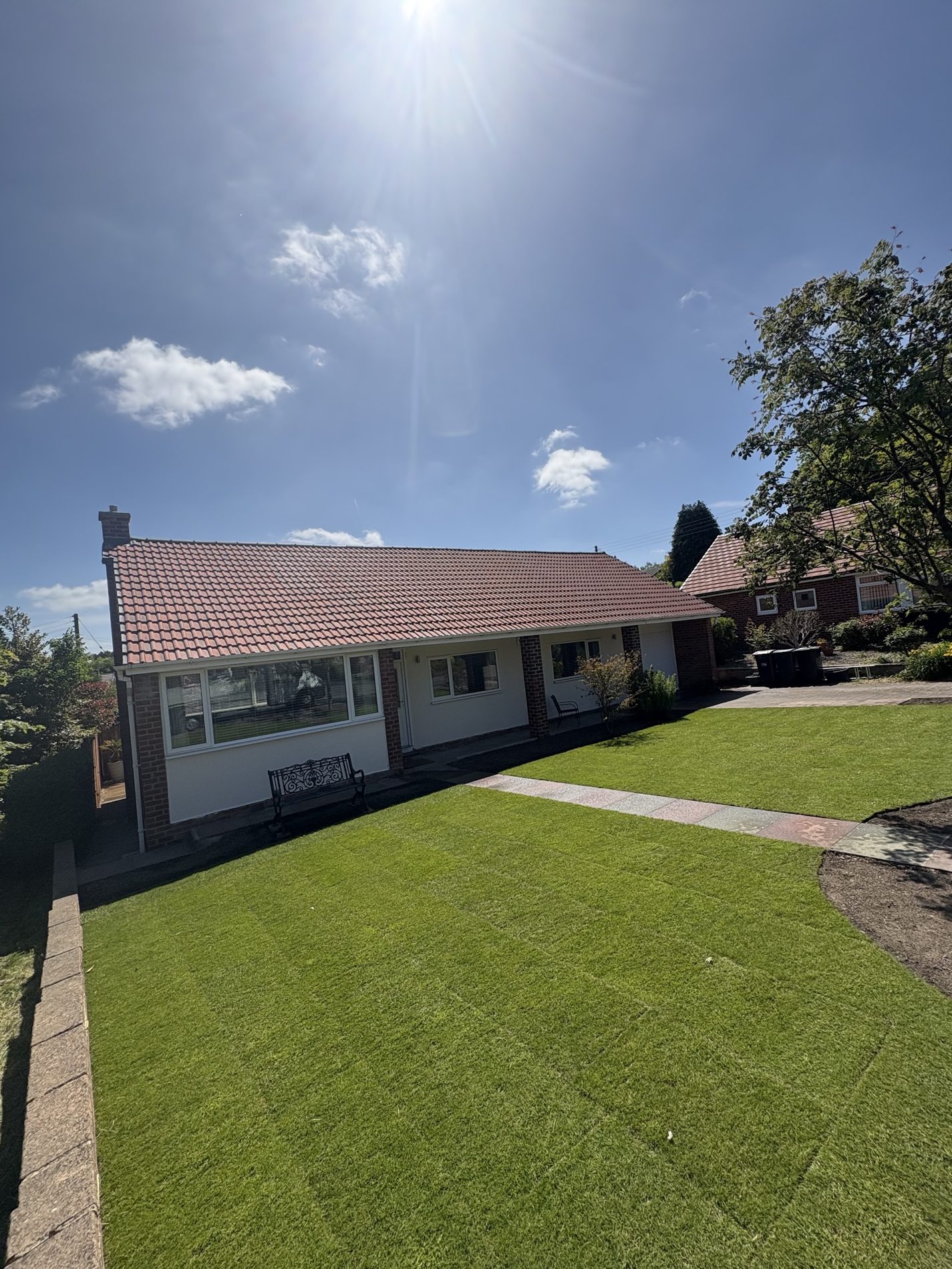 A bungalow with a new lawn and a curving path in bright sun